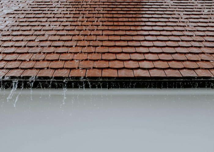 Brown roof tiles with rainwater cascading down, showcasing architectural texture and detail.