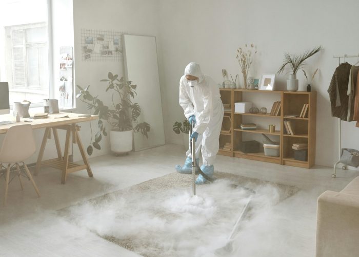 A person in protective gear disinfects a room with smoke, ensuring safety against germs.