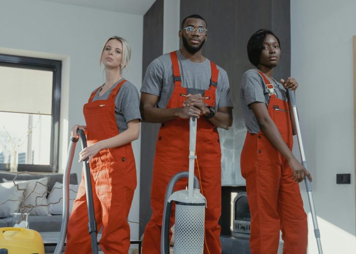 Three cleaners in uniform with equipment in a modern home interior, showcasing teamwork and professionalism.