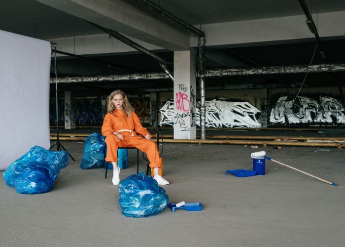 Portrait of a woman sitting in a warehouse, surrounded by graffiti and cleaning tools.